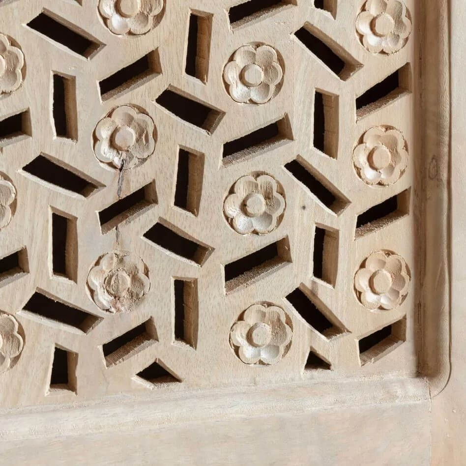 Close-up of a light natural wood carved screen or wall panel with repeating floral and geometric cutout patterns.