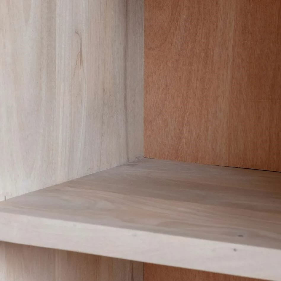 Close-up of a wooden shelf corner with light natural wood grain on the shelf and back panel, and a medium warm brown wood panel on the right side.