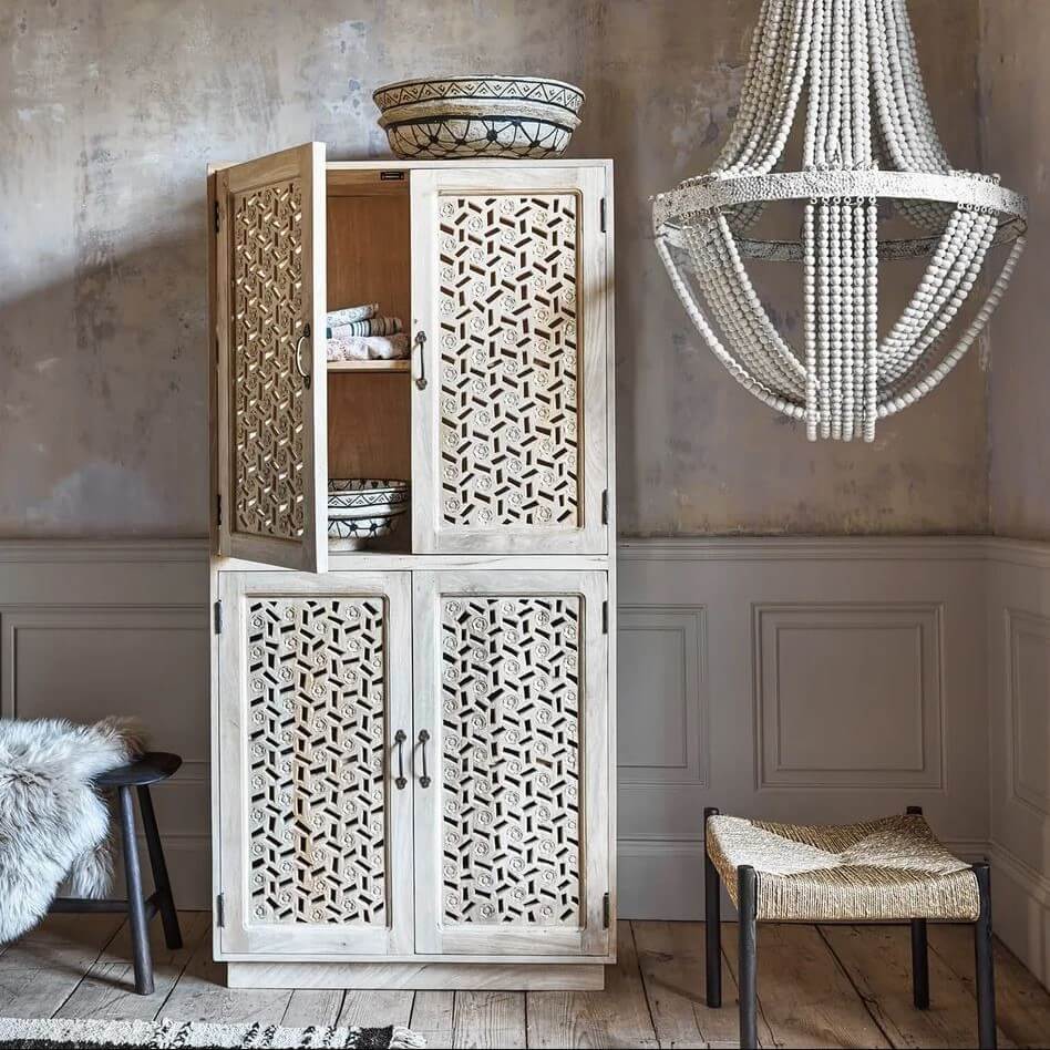 A tall, rustic white wooden cabinet with intricate geometric cutout patterns on the doors.