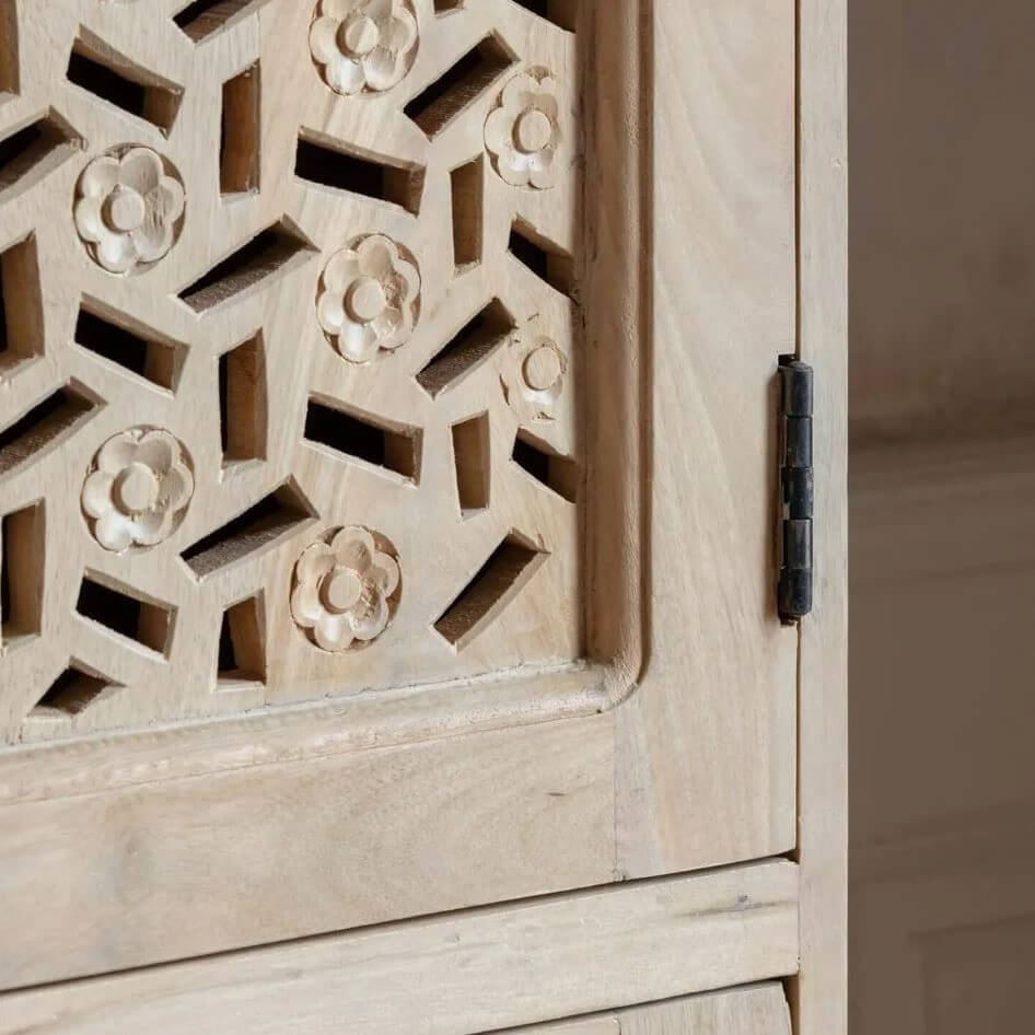 Close-up of a light natural wood cabinet door with intricate geometric cutouts and carved floral motifs, featuring a black metal hinge.