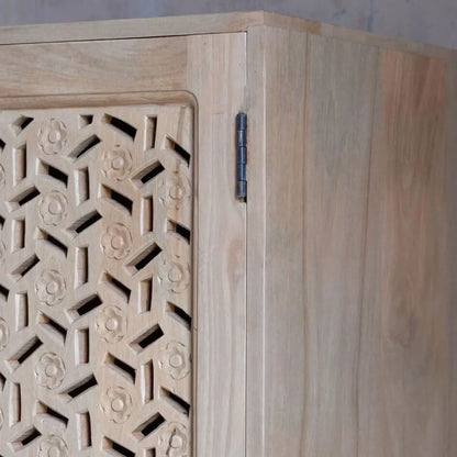 Close-up of a light natural wood cabinet corner showing a carved geometric patterned door panel, a dark metal hinge, and the side wood grain.